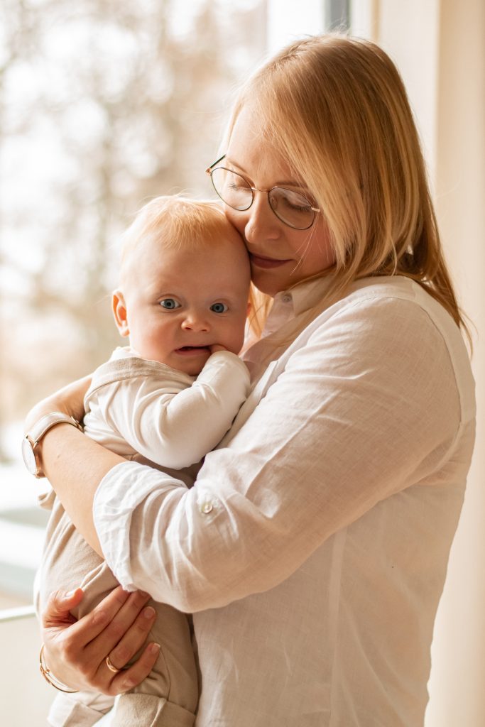 Mutter steht mit Baby auf dem Arm vor dem Fenster